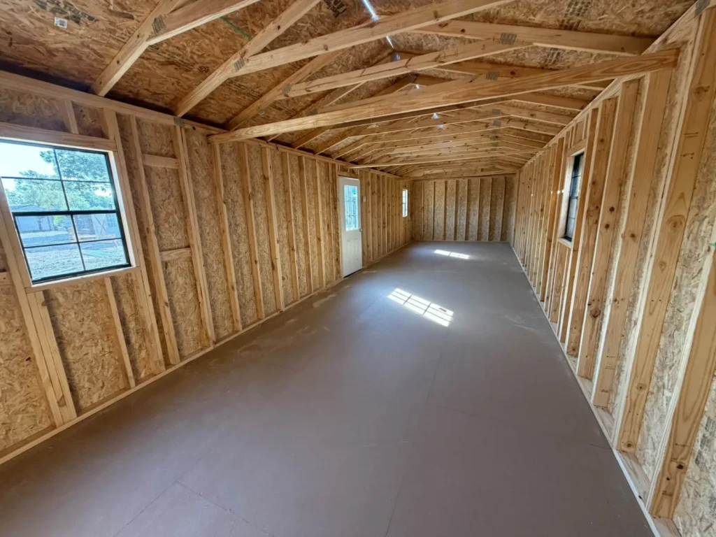 Long open floor inside a 12x40 portable building with exposed framing, roof trusses, and sunlight from side windows, ready to finish as a workshop or office