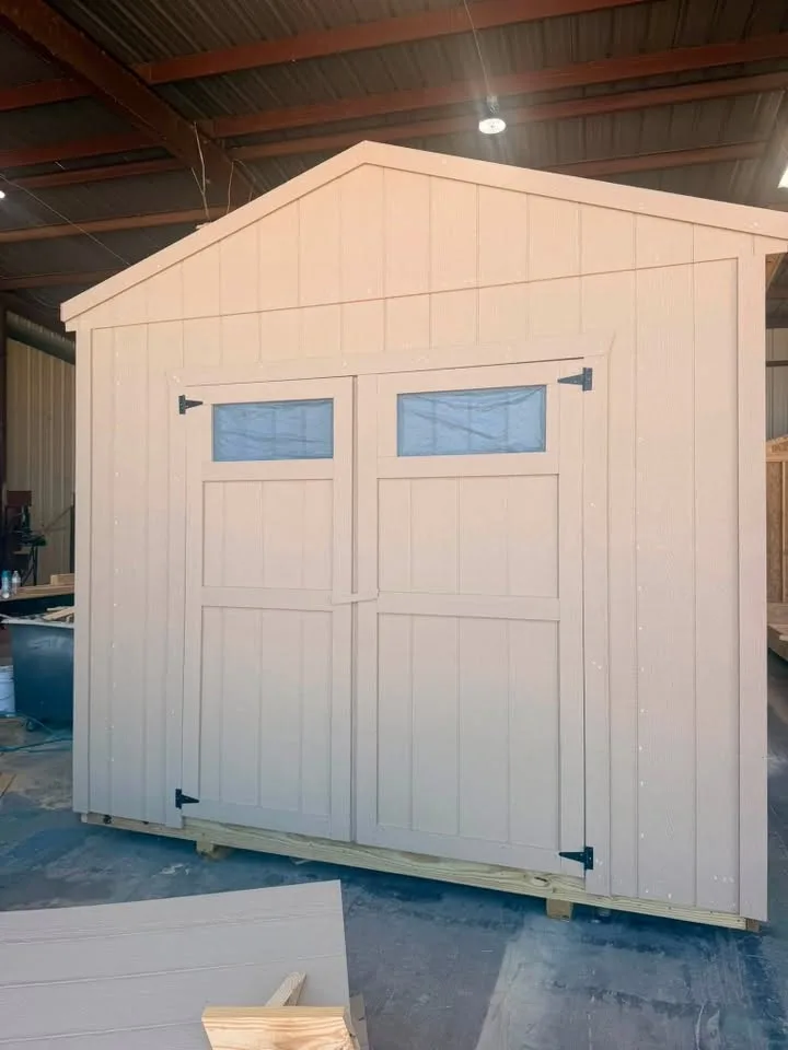 Cream-colored utility shed with double doors topped by small transom windows, inside the build shop