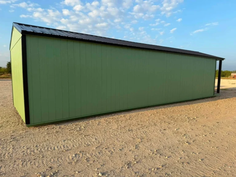 Long green portable building with black trim and a black metal roof on a gravel lot