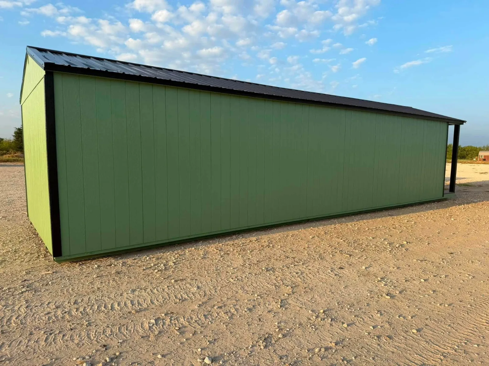 Long green portable building with black trim and a black metal roof on a gravel lot