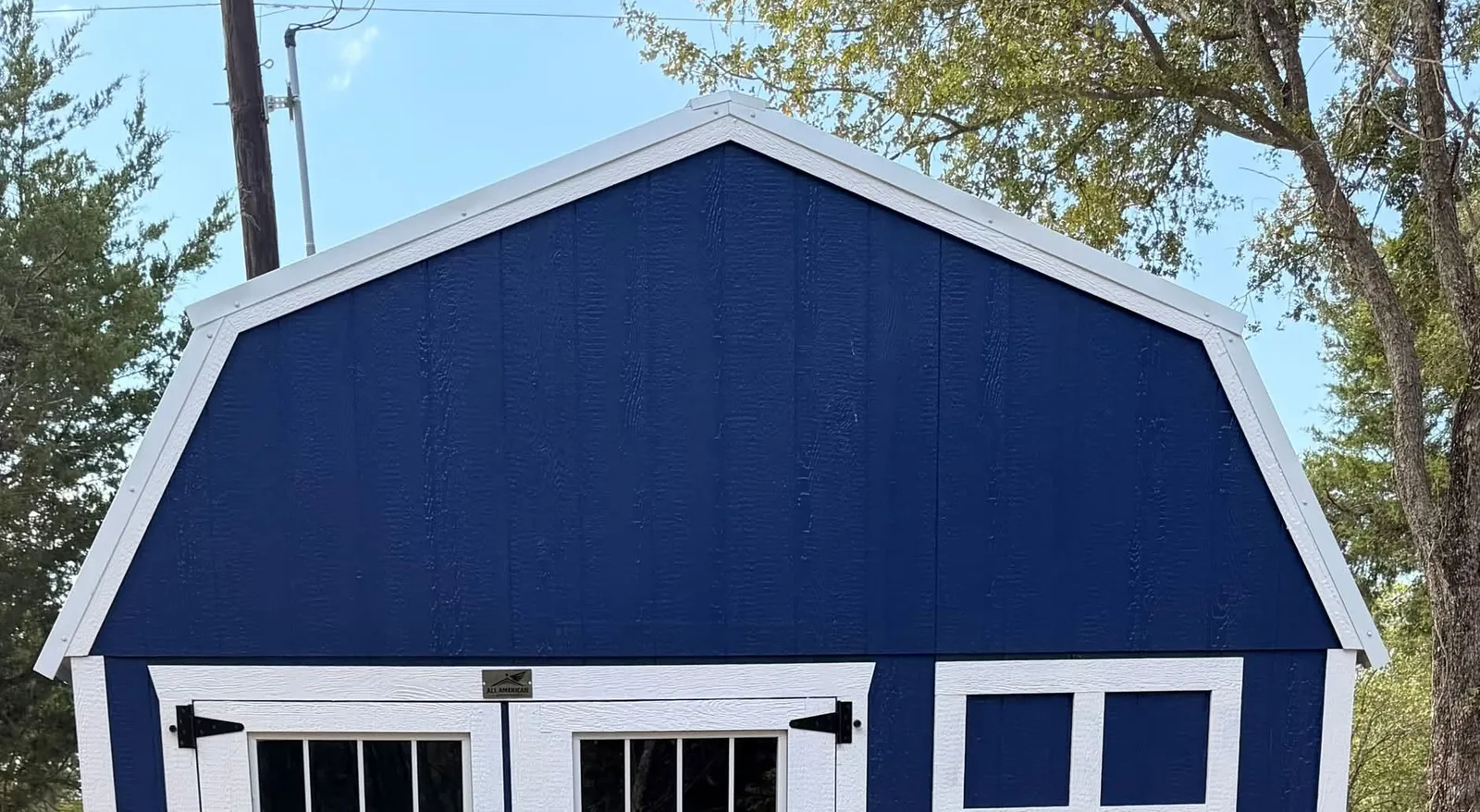 Navy blue 12x20 lofted barn with white trim, a gambrel roof, double doors with transom windows, and a white-framed window, delivered near Corsicana