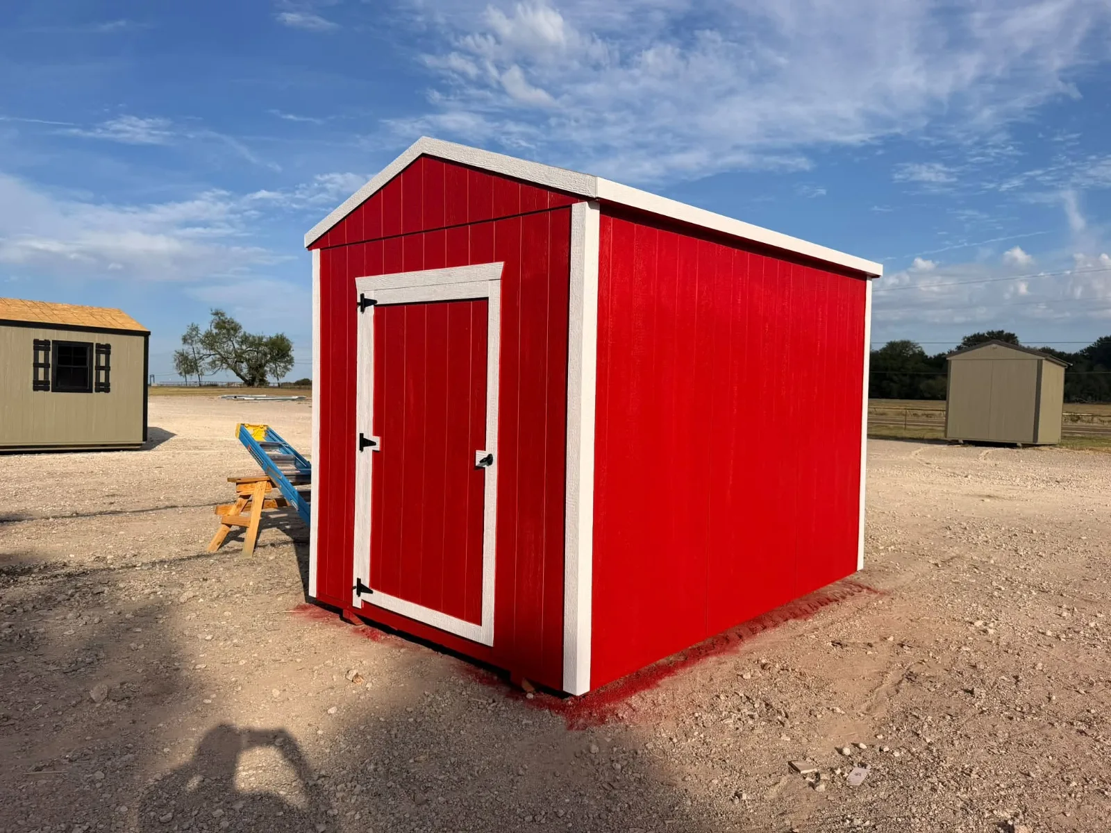 Red storage shed with white trim, a single white door, and a metal roof on the sales lot