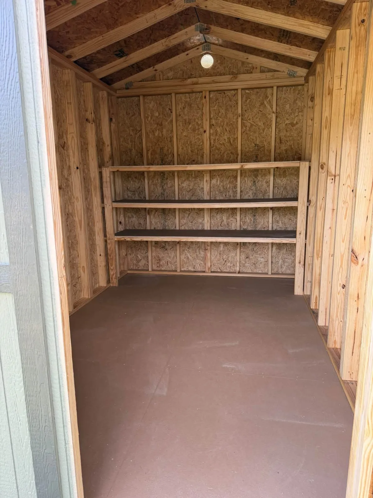 Inside a storage shed with built-in wooden shelves along the back wall and a painted floor