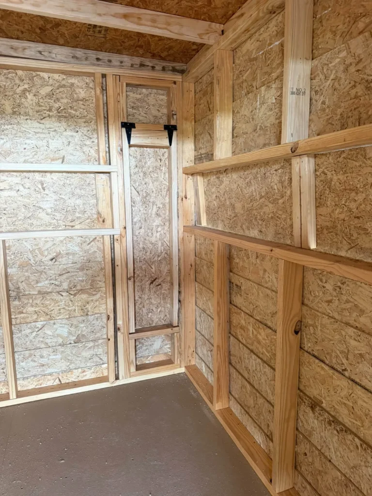 Inside a portable building: exposed wood framing, a loft ledge, and a wall-mounted ladder above a painted floor